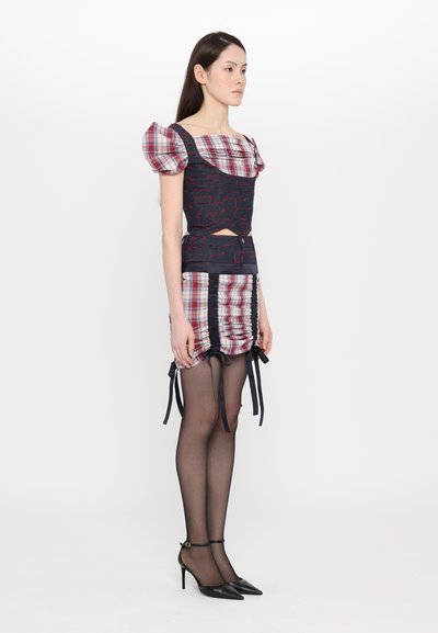 Multi-patterned dress with a fitted bodice and puff sleeves. Dark blue and red fabric, plaid skirt, ruched details, and tie accents.