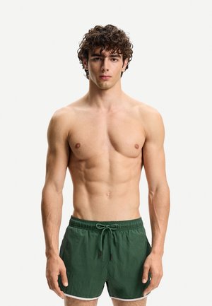 Grüne Schwimmshorts mit elastischem Bund und Kordelzug. Leichtes Material, kniehoch, mit weißem Saum entlang des Rands.