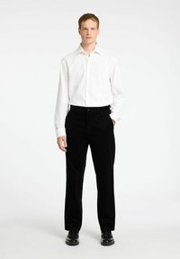 Bela srajca z dolgimi rokavi v kombinaciji s črnimi kordnimi hlačami. Oblikovanje v slim fit; gladka tekstura tkanine; srajčna ovratnica. Črne usnjene čevlje.