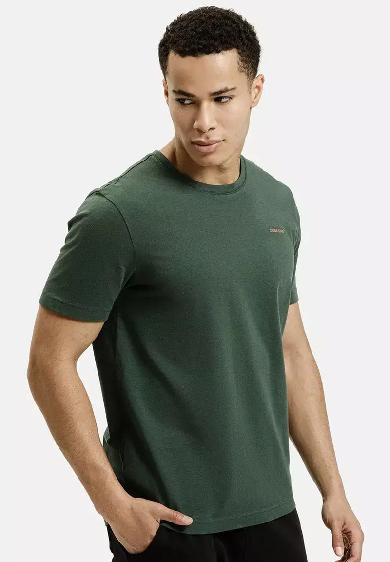 Ciemnozielona bawełniana koszulka z krótkim rękawem, okrągłym dekoltem i małym pomarańczowym logo na piersi. Gładka faktura, luźny krój.