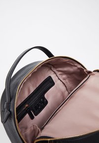 Sort tekstureret læderhåndtaske med en gylden lynlås, der har en blød lyserød inderside og en sort lynlåslomme indeni.