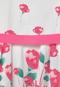 Tissu blanc avec un motif floral de fleurs roses et vertes. Comprend une ceinture en ruban rose vif et des plis froncés sous la taille.