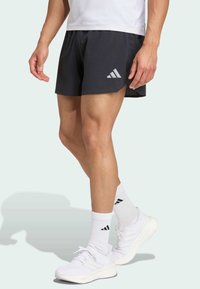 Black athletic shorts with mesh side panels and an Adidas logo. Paired with white sneakers and crew-length socks featuring black accents.