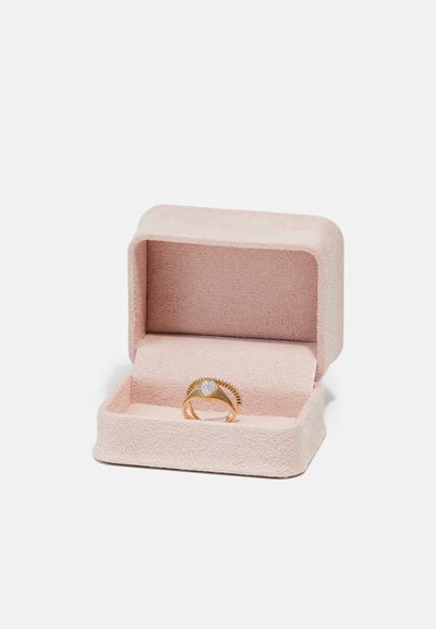Gold ring with a heart-shaped design and small clear stones, displayed in a soft pink suede box with a removable lid and a plush interior.
