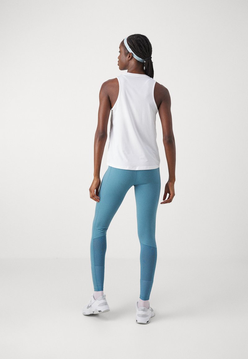 Top blanco sin mangas con cuello redondo, combinado con leggings azules ajustados con un panel estampado, usados con zapatillas blancas.