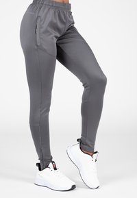 Grijze sportbroek met een elastische tailleband, een zijrits zak en een taps toelopende pasvorm, gecombineerd met witte sportschoenen.