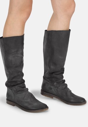 Botas de cuero negro hasta la rodilla con un ajuste holgado, punteras puntiagudas y suelas planas. El material parece ligeramente texturizado y mate.