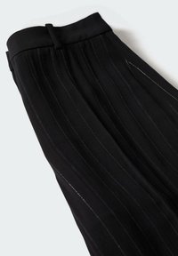 Pantalons ajustés noirs à rayures, avec ceinture et passant de ceinture, posés à plat sur un fond clair.