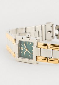 Ceas de mână cu cristal de cuarț, cu carcasă rectangulară din argint, cadran verde, accente aurii și o brățară metalică în două tonuri cu linkuri lustruite și periate.
