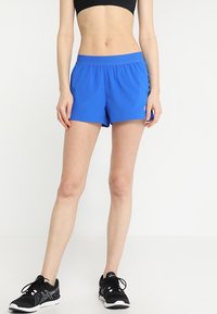 Blå träningsshorts med elastisk midjeband, en slät yta och längd till mitten av låret. Matchad med svarta löparskor.