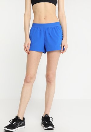 Blaue Sportshorts mit einem elastischen Bund, einer glatten Textur und einer Länge bis zur Mitte des Oberschenkels. Kombiniert mit schwarzen Laufschuhen.