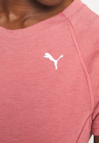Short-sleeve shirt in light pink fabric, featuring a PUMA logo in white, with smooth texture and contrasting seams along the neckline.