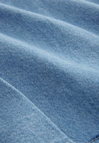 Lichtblau denim stof met een gladde textuur, gekenmerkt door diagonale naden en een consistente ribstof weefstructuur.