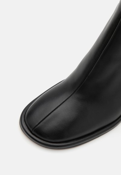 Svart läderankelboot med en slät yta, rund tå, enkel sömdetalj och minimalistisk design.