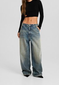 Ljusblå denim jeans med vida ben och en blekt yta, hög midja och sidofickor; matchade med en kort svart ribbad långärmad topp.