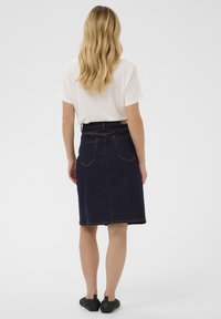 Tamsiai skalbto džinso midi sijonas su tiesiu kirpimu, turintis kišenes gale ir šviesias siūles. Dėvimas su balta marškinėlių ir juodais batais.