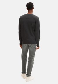 Kohlegrauer Pullover mit Rundhalsausschnitt, aus weichem Stoff, kombiniert mit hellgrauen Jeans und weißen Sneakern. Die Ansicht zeigt die Rückseite des Outfits.