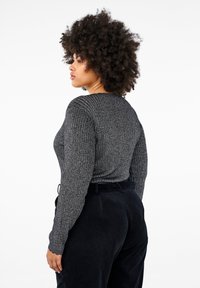 Grå ribbad långärmad tröja med rund halsringning, bärs med svarta manchesterbyxor. Tyget har en texturerad, något glänsande yta.