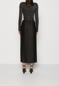 Černý top s dlouhým rukávem s třpytivou texturou v kombinaci s plisovanou černou sukní. Má přiléhavý pas a ozdobný pás s logem. Černé sandály na podpatku s pásky.