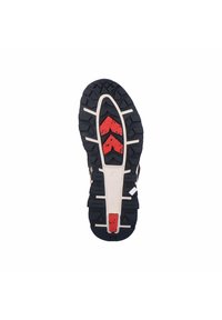Semelle de chaussure de trail running avec une semelle en caoutchouc noir, des crampons profonds, des accents rouges et blancs, et des motifs texturés pour l'adhérence.