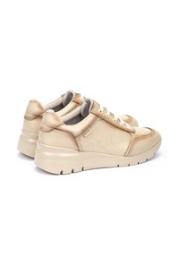 Zapatillas de cuero beige con textura suave, punta redondeada y suela de goma gruesa. Presentan un diseño con cordones y detalle de logo en el lateral.