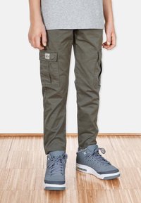 Olivgrön cargobyxor med sidfickor, en tygapplikation, matchade med grå sneakers med texturerade detaljer och snörning.