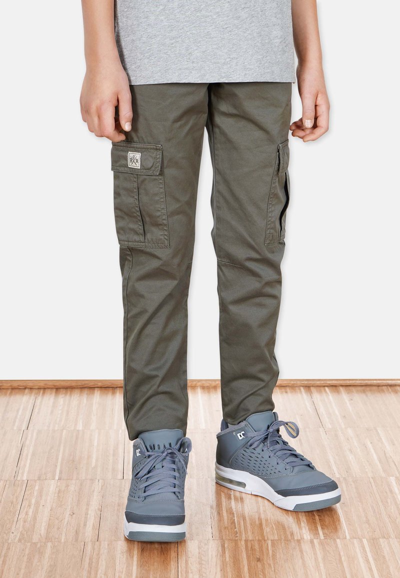 Olivgrön cargobyxor med sidfickor, en tygapplikation, matchade med grå sneakers med texturerade detaljer och snörning.