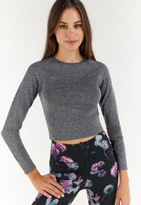 Grijze cropped langwerpige top met gestructureerde stof, voorzien van raglanmouwen. Gecombineerd met zwarte leggings versierd met kleurrijke bloemenpatronen.