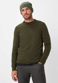 Maglione verde oliva a maniche lunghe con collo rotondo, polsini a coste e finitura testurizzata, abbinato a pantaloni grigi con texture e un berretto coordinato.
