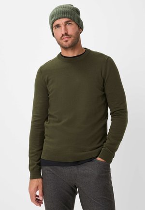 Pull à manches longues vert olive avec col rond, poignets côtelés et finition texturée, associé à un pantalon gris texturé et un bonnet assorti.
