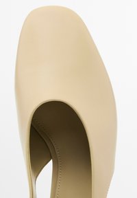 Scarpa in pelle beige con punta tonda e design laterale aperto. Texture liscia e dettagli di cucitura minimi.