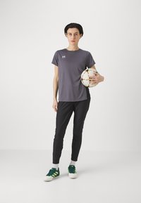 Hallitus halli T-särk, lühikeste varrukatega, mustad spordipüksid, rohelised jalgpalliketsid, hoiab mitmevärvilist jalgpall,” ühetaolise taustaga.