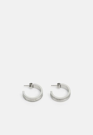Boucles d'oreilles en argent en forme de créoles présentant une surface lisse et une rangée de petites pierres claires le long du bord inférieur, avec une fermeture à tige.