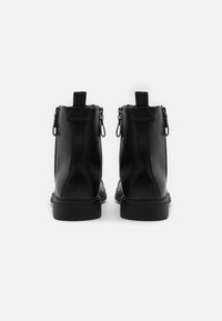 Botas de tobillo de cuero negro con un acabado liso, que cuentan con una cremallera lateral y una lengüeta, montadas sobre una suela plana de goma.