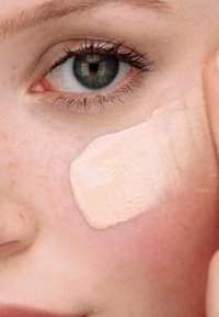 Fond de teint liquide appliqué sur la joue, couleur beige avec une texture lisse. La peau présente un ton naturel, clair avec des taches de rousseur et une légère rougeur.