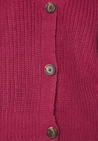 Knitted burgundy cardigan featuring ribbed texture, five buttons with a dark finish, and a fitted hem.