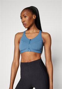 Μπλε αθλητικό σουτιέν με μπροστινό φερμουάρ, που διαθέτει εφαρμοστή σχεδίαση, φαρδιές τιράντες και λεία υφή. Συνδυάζεται με μαύρα κολάν με ψηλή μέση.