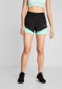 Svarta atletiska shorts har en lagerdesign med ett bredare midjeband och inbyggd myntgrön foder. Bärs med svarta sneakers.