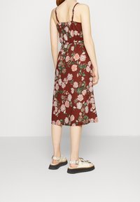 Kukkakuvioinen midi-mekko burgundin värissä, jossa on vaaleanpunaisia ja vihreitä ruusukuoseja, ohuita olkaimia ja vyötäröllä vyö. Yhdistetty vaaleanbeigeihin sandaaleihin.