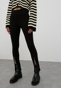 Zwarte leggings met zijritsen, gecombineerd met een zwart-wit gestreepte cropped sweater; glad materiaal, slim fit en enkel lengte ontwerp.