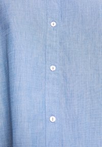 Tissu bleu clair texturé avec une rangée verticale de trois boutons blancs cousus au centre.