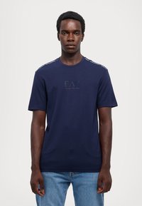 Navyblauwe katoenen T-shirt met korte mouwen, ronde hals, geborduurd logo op de borst en contrasterende schouderaccenten.