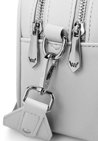 Bílá taška z faux kůže se stříbrným zipem a kováním. Obsahuje D-kroužek pro připevnění s hladkou, matnou texturou a ostrými akcenty.