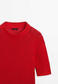 Pull en maille rouge à manches courtes, avec un col rond et une texture à maille ouverte. Détails en côtes au niveau du col et des manches.