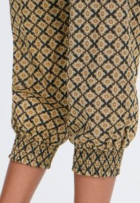 Tissu noir avec un motif de diamants en or et crème, featuring des poignets élastiques à l'ourlet pour un look froncé. Design léger et texturé.