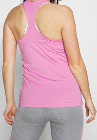 Donna che indossa un top racerback rosa chiaro sopra un reggiseno sportivo bianco e leggings grigi con strisce laterali rosa, in piedi di spalle rispetto alla fotocamera.