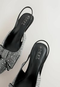 Melni slingback apavi, rotāti ar spīdīgiem rhinestones, ar joslu detaļu priekšā un gludu, teksturētu zolīti.