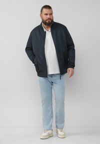 Marine bomberjack met een rechte kraag, zijzakken en een ritssluiting; gecombineerd met lichtblauwe jeans en witte sneakers.