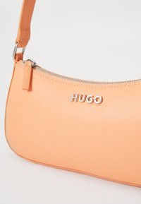 Borsa a spalla color pesco in pelle testurizzata. Presenta una cerniera argentata e il logo "HUGO" impresso sul davanti. Forma liscia e curva.