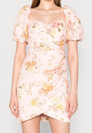 Woman wearing a pale pink floral dress with puff sleeves and a sweetheart neckline, featuring a ruched, wrap-style skirt.